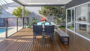 Une terrasse extérieure moderne, dotée d’une plateforme en bois, d’une table à manger avec des chaises et d’un barbecue.