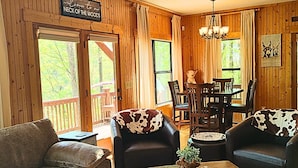 Interior acogedor de una cabaña con paredes de madera, un comedor y un letrero que dice 'Welcome to Neck of the Woods'.