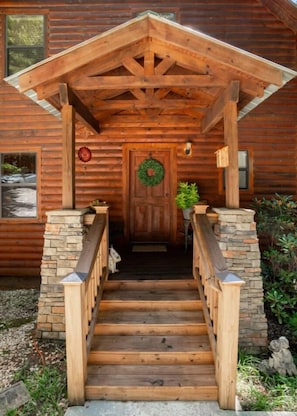A wooden cabin with a stone staircase leading to a door with a wreath.