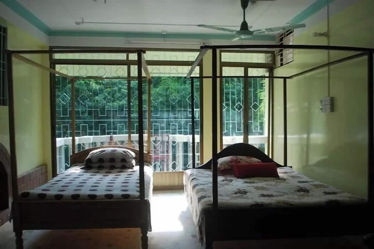 Ein Zimmer mit zwei Betten, einem Deckenventilator und Blick auf Grünflächen.