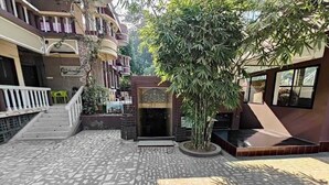 Ein Innenhof mit Fliesenboden, einer Treppe, einer kleinen Gartenanlage mit Baum und einem Gebäude mit Balkon.