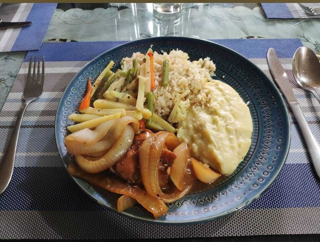Un plato de comida con arroz, verduras y un acompañamiento sobre una mesa con un mantel individual.