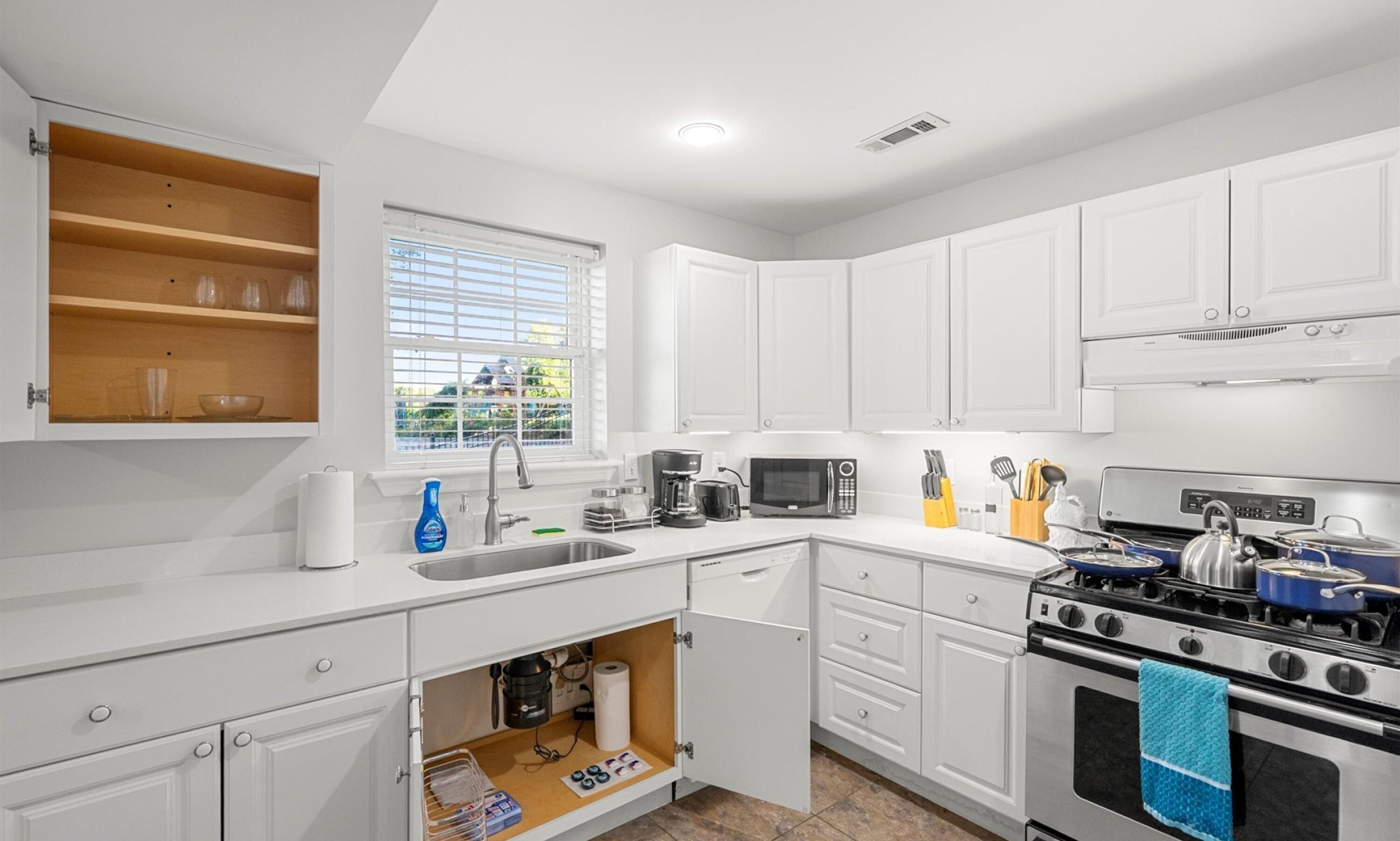 A modern kitchen with white cabinets, a sink, a stove, and a microwave.