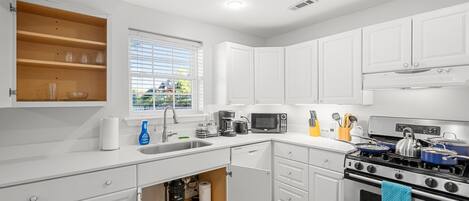 A modern kitchen with white cabinets, a sink, a stove, and a microwave.