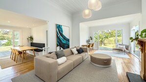 Een ruime woonkamer met een grote bank, een eettafel en een televisie. Een groot raam biedt uitzicht op het omliggende landschap.