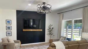 Una sala de estar moderna con una pared de acento negra, un televisor de pantalla plana, un sofá grande y un comedor con mesa y sillas.
