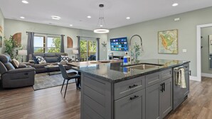 Uma cozinha moderna com uma ilha grande, uma sala de jantar com sofá e uma sala de estar com lareira.