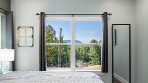 Quarto com uma janela grande, uma cama com manta branca texturizada, mesa de cabeceira e espelho na parede.