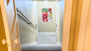 Un pasillo con alfombra roja que presenta un logotipo blanco, un cartel en la pared y una escalera que conduce a otra habitación.