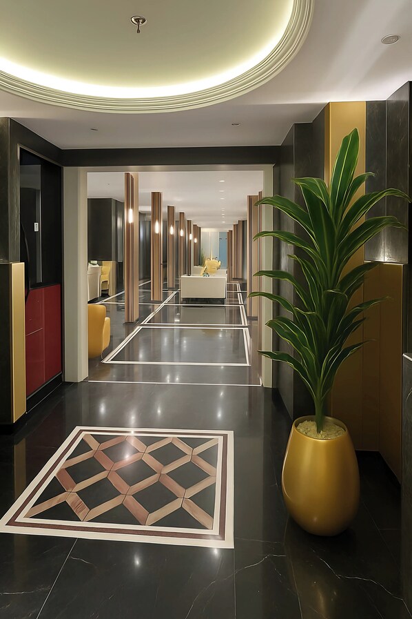 En modern hotellobby med ett reflekterande golv, en central sittgrupp och en stor krukväxt.