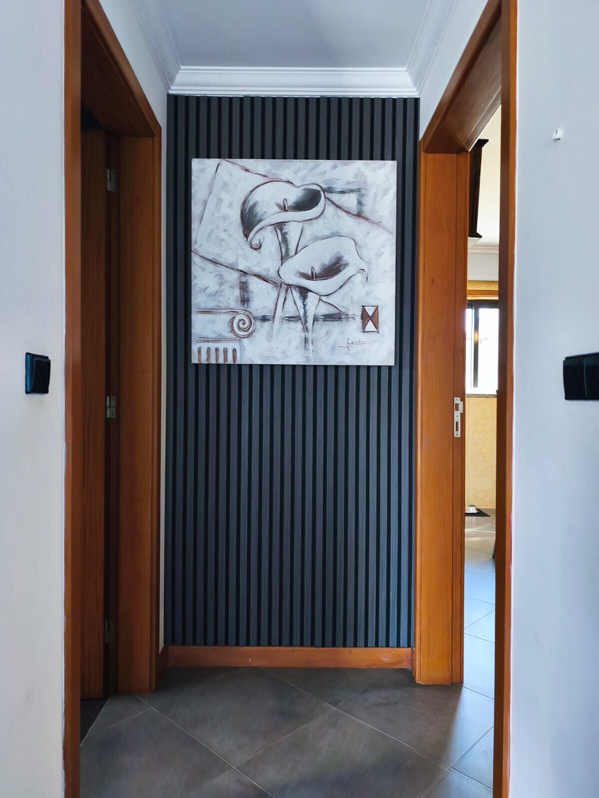 Un pasillo con un cuadro abstracto moderno en la pared, puertas de madera y suelo de baldosas.