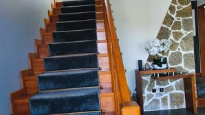 A staircase with wooden steps and a carpeted handrail, leading to a stone wall and a small seating area with a plant.