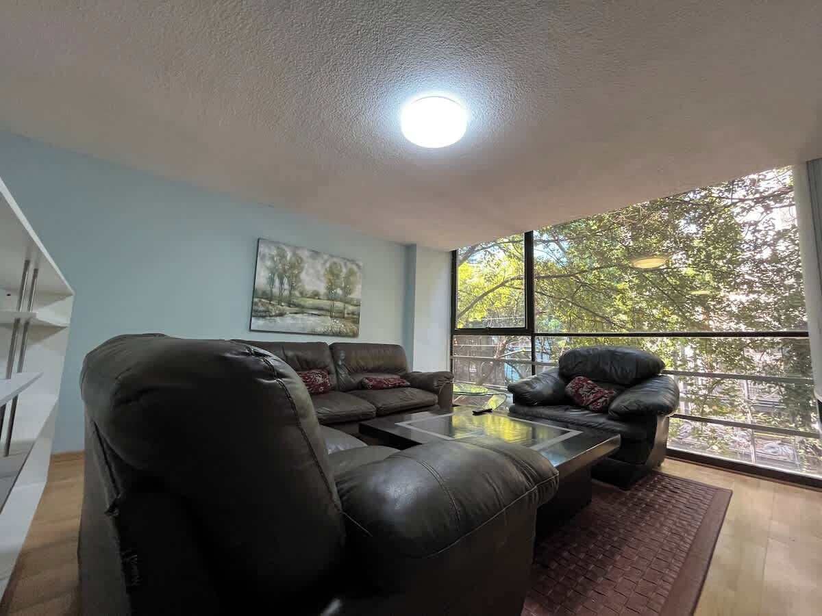 A living room with a sofa and armchair, a coffee table, and a painting on the wall.