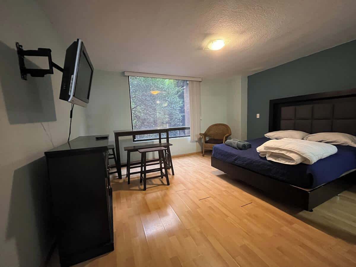 A bedroom with a bed, a desk, a chair, and a TV mounted on the wall.