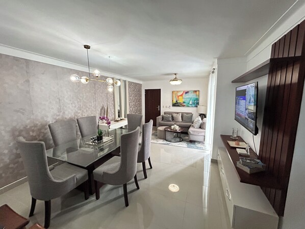 Una sala de estar moderna con un televisor de pantalla plana, una zona de comedor con una mesa de vidrio y un juego de sofá.