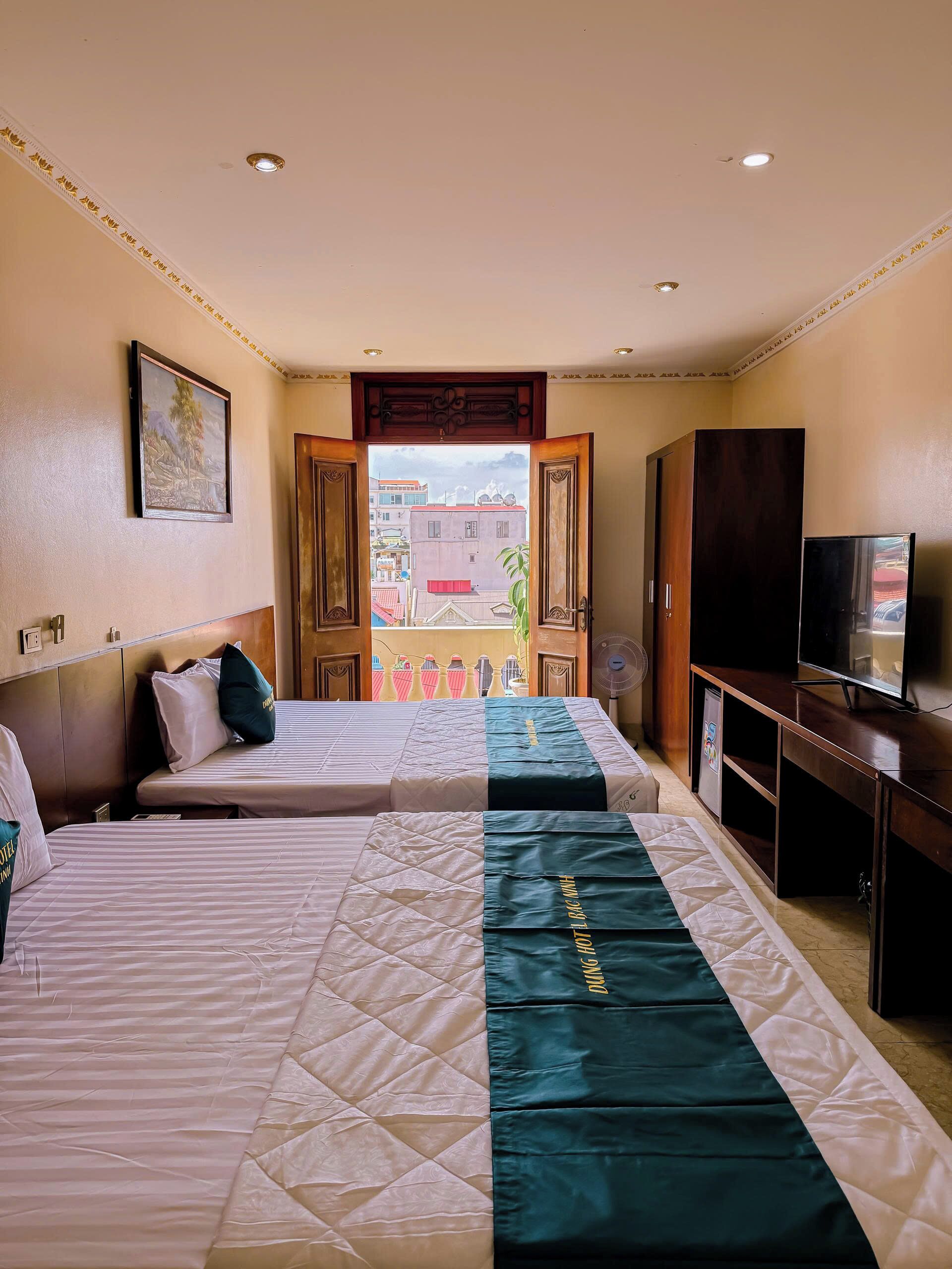 A hotel room with two beds, a television, a wardrobe, and a balcony with a view of buildings.