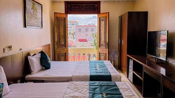 A hotel room with two beds, a television, a wardrobe, and a balcony with a view of buildings.