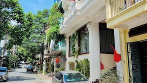 A street view with a parked car, buildings with balconies, and a flag. - Sky 2 Hotel (Kinh Bac)