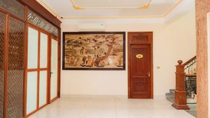 A hallway with a traditional wooden door, a large framed artwork on the wall, and a staircase with a wooden railing. - Sky 2 Hotel (Kinh Bac)