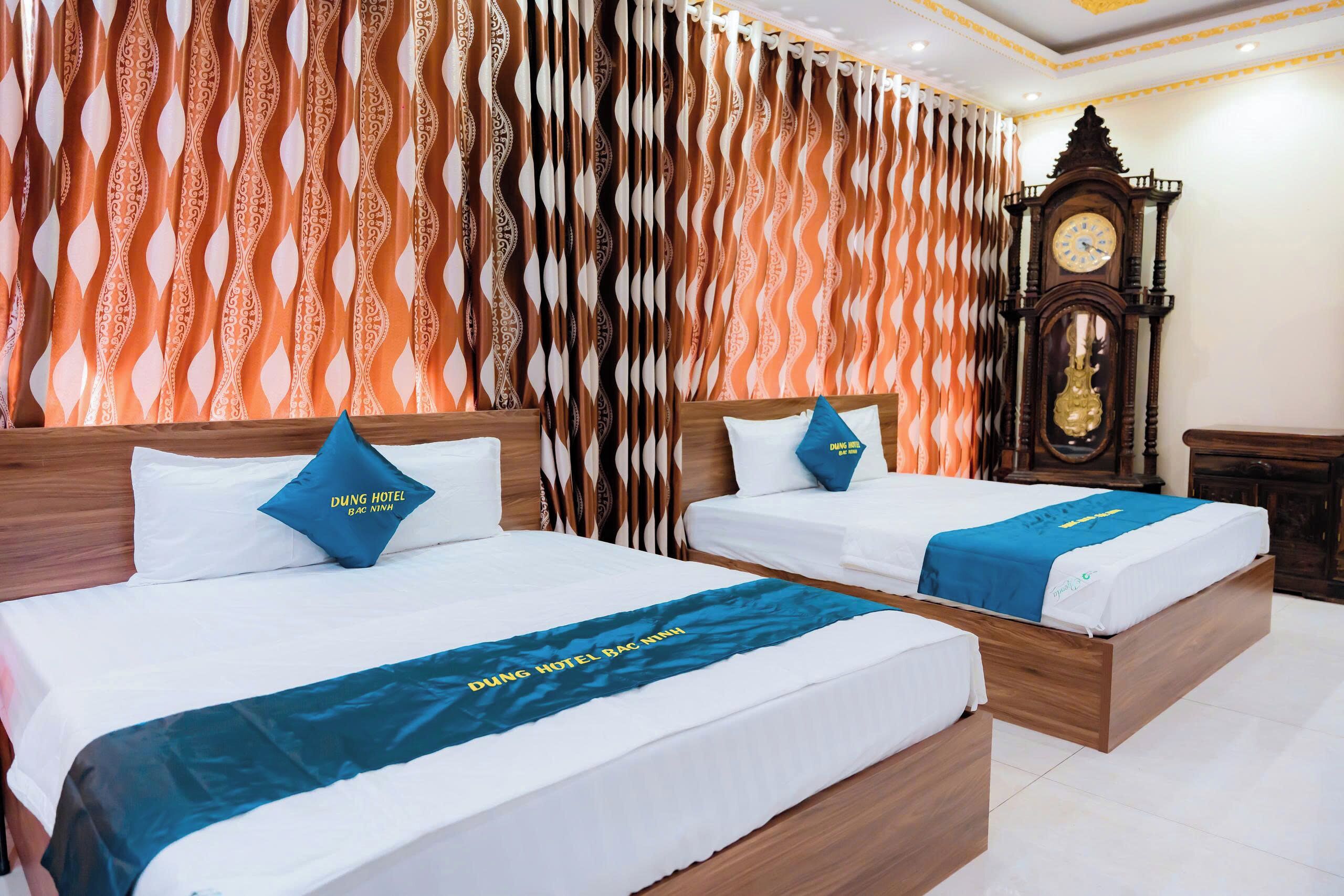 Habitación de hotel con dos camas, cada una con cubrecama y almohadas azules, y una cortina estampada.