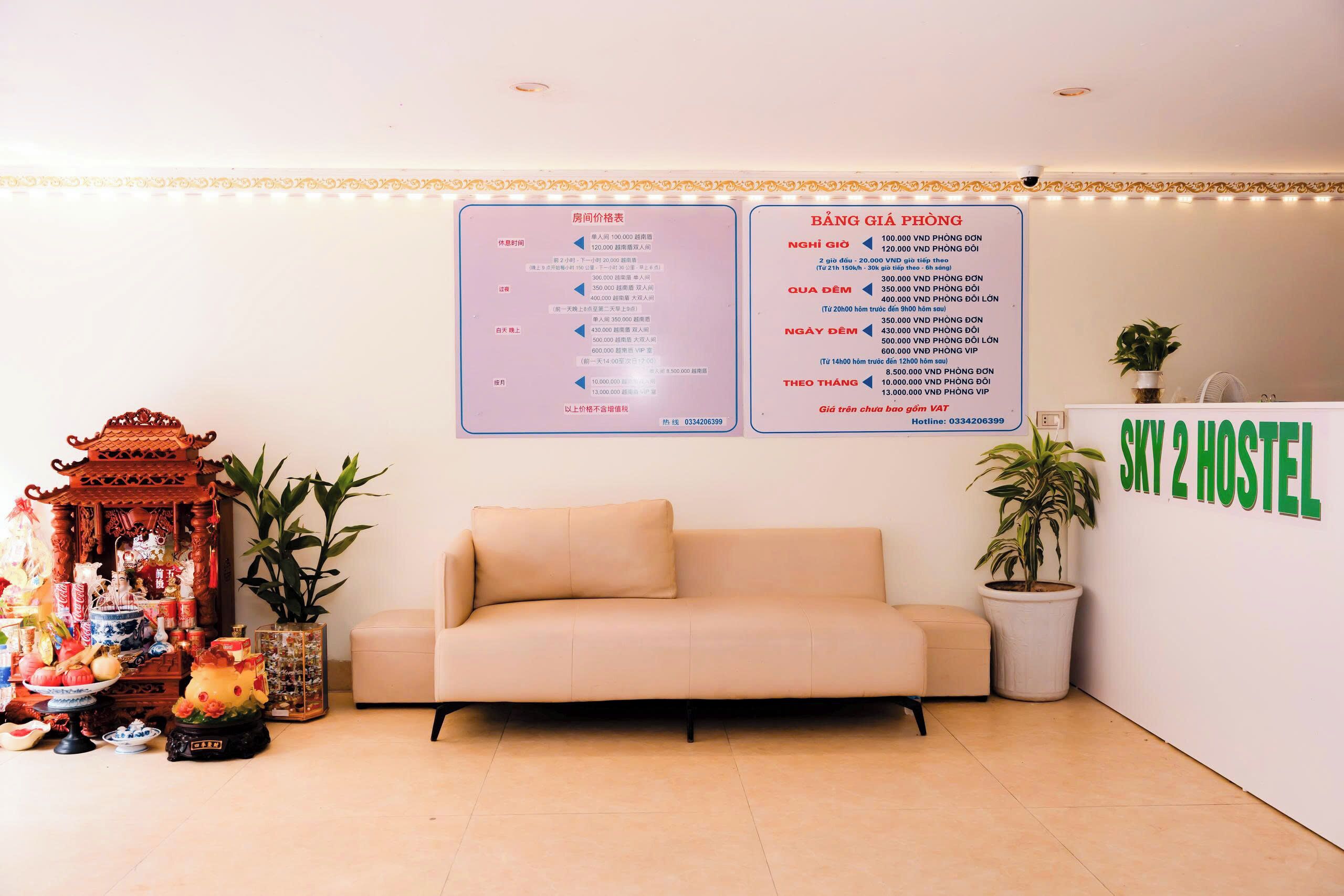 A hotel reception area with a sofa, a shrine, and a wall with a price list.