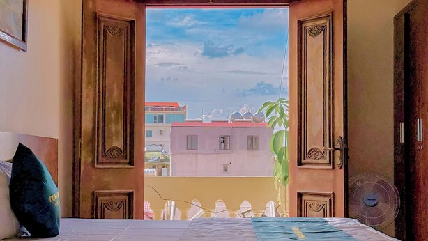 A hotel room with a bed, a view of buildings outside, and a wooden door with intricate carvings. - Sky 2 Hotel (Kinh Bac)