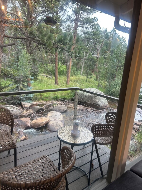 A deck with wicker furniture overlooking a natural landscape with a stream and trees. -  Hot Tub! Charming 3-bedroom house in Estes Park- On the River! (Estes Park)