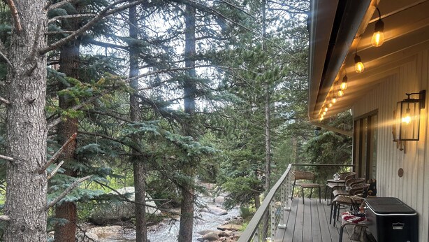 Terraza de madera con mobiliario exterior con vista a un río y un bosque.