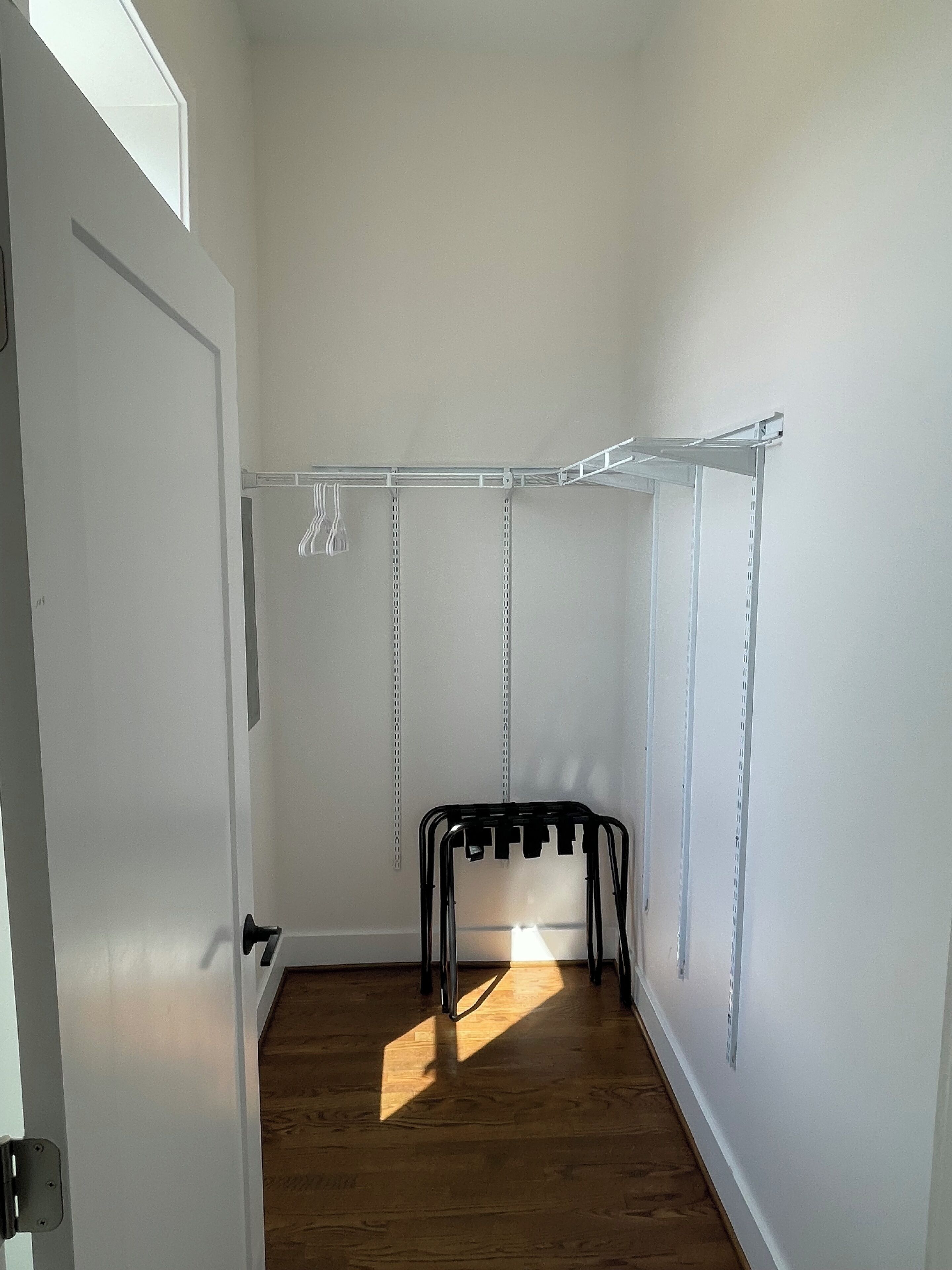 A walk-in closet with a metal shelving unit, a door, and wooden flooring.