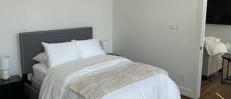 A neatly made bed with white linens in a room with wooden flooring and a grey headboard.
