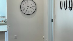 A hallway with a wall-mounted clock, a door, and a coat rack.