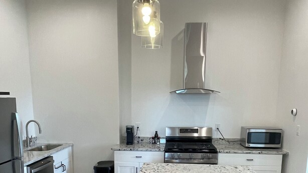 A modern kitchen with white cabinetry, a granite countertop island, stainless steel appliances, and a hanging pendant light.