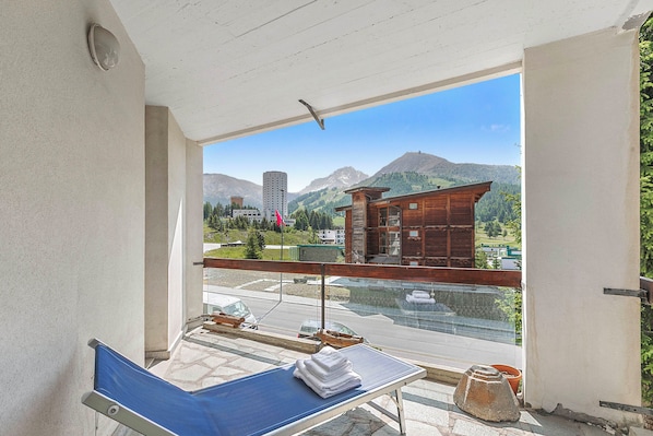 Une chambre avec balcon, une vue sur les montagnes, un bâtiment en bois et une route où circulent des véhicules.