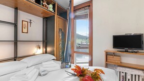 Una habitación de hotel con cama, televisor, ventana con vistas y repisa con objetos decorativos.