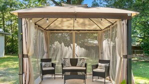 A covered outdoor seating area with two chairs and a bench, surrounded by sheer curtains and a canopy. - Escape by Beaches & Blue Angels (Pensacola)