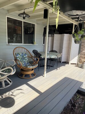 A covered patio area with a wooden deck, wicker chairs, a table, and hanging planters.