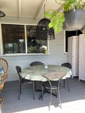 A covered patio with a round table and chairs, a hanging black light fixture, and a potted plant.