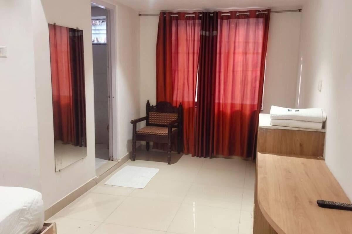 A hotel room with a bed, a wooden bench, a chair, a small table, and a mirror.