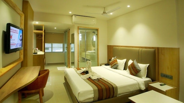 A hotel room with a large bed, a desk, a TV, and a bathroom visible through a glass door.