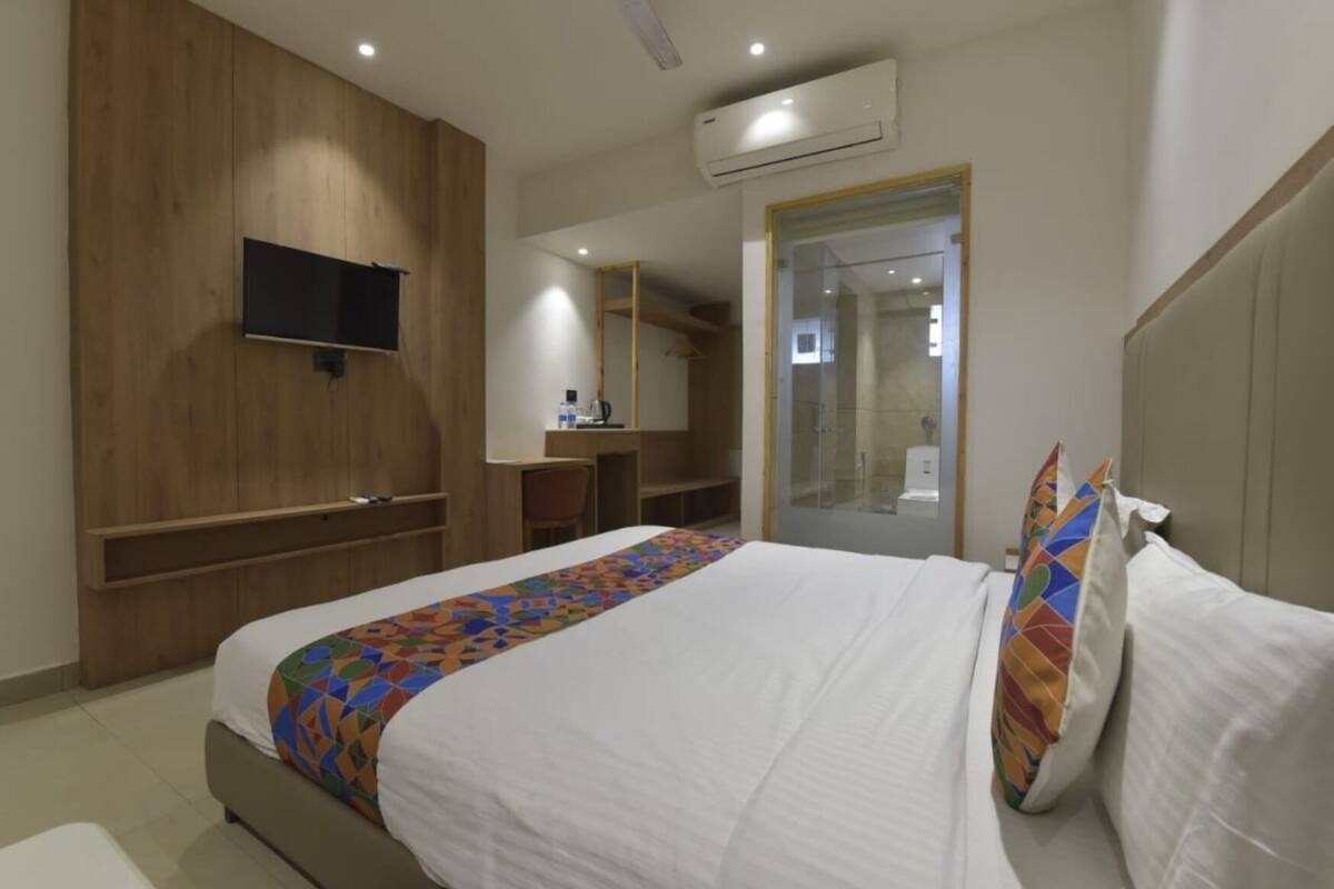 A hotel room with a bed, a TV mounted on the wall, a shower area, and a small desk with a chair.