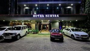 A hotel named HOTEL SURYA with a modern facade, a covered entrance, and three cars parked in front.