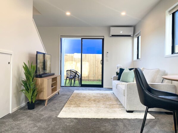 A modern living room with a sofa, a coffee table, a black chair, a wooden cabinet, and a potted plant.