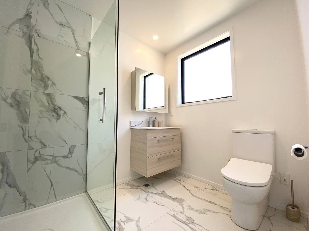 Ein modernes Badezimmer mit Duschkabine aus Glas, Marmorboden, weißer Toilette und einem Holzwaschtisch mit Spiegel.