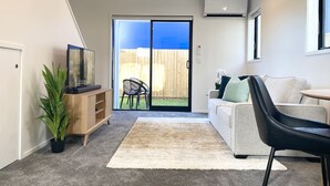 Una sala moderna con un sofá, una mesa de centro, una silla negra, un mueble de madera y una planta en maceta.