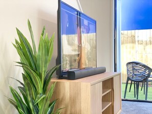 A room with a TV on a wooden stand, a potted plant, and a view of a backyard with a chair.