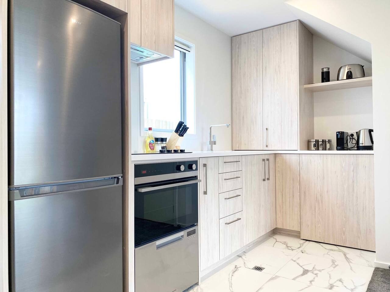 A modern kitchen with stainless steel appliances, wooden cabinets, and a marble floor.