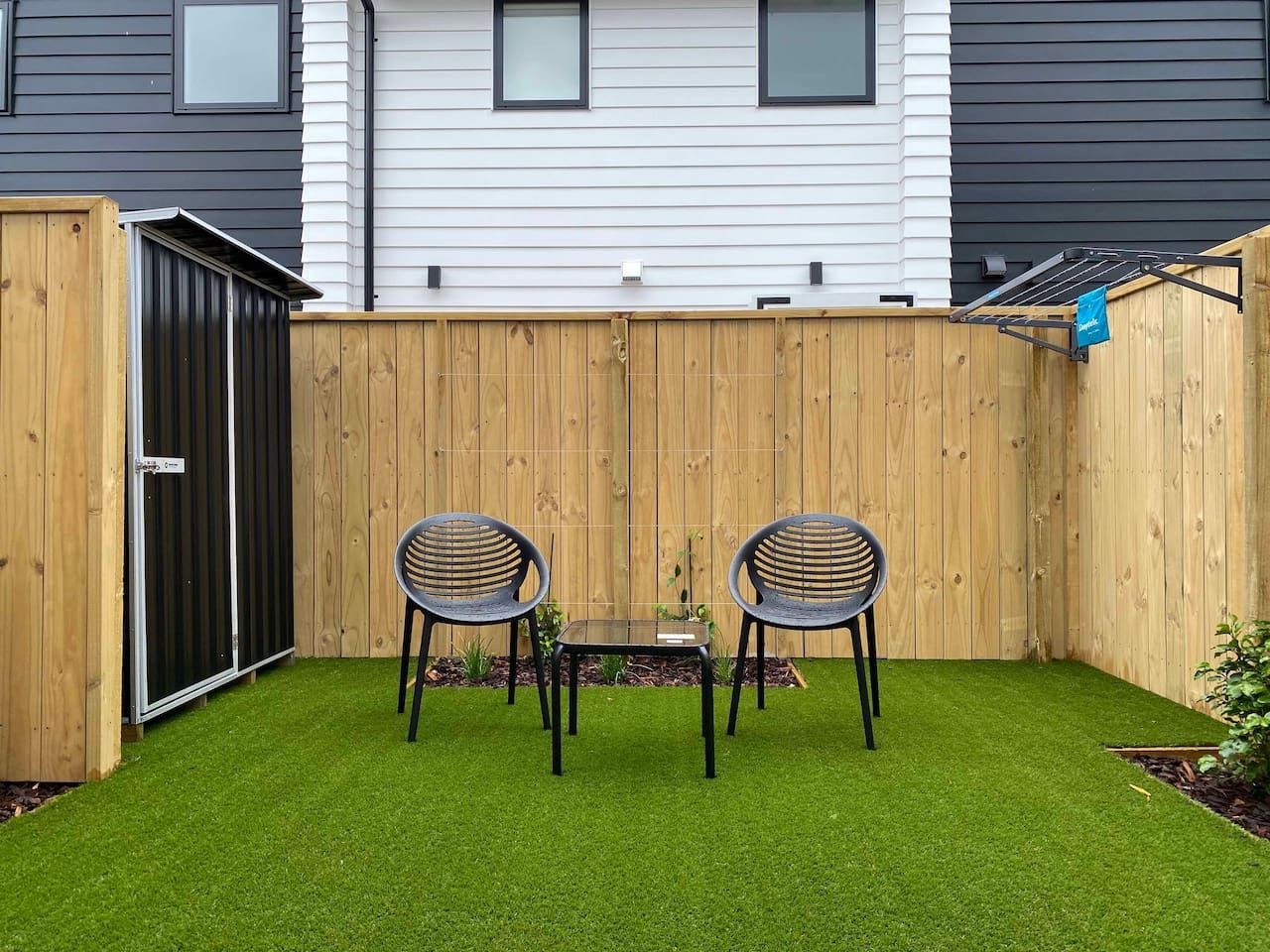 A fenced backyard with artificial grass, two chairs, and a table.