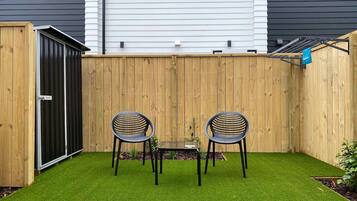 A fenced backyard with artificial grass, two chairs, and a table.