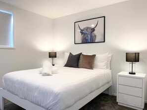 Una camera d'albergo con un letto grande, biancheria da letto bianca, due comodini con lampade, un quadro appeso alla parete e una finestra con tende.
