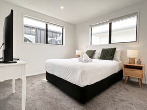 A modern bedroom with a large bed, two bedside tables, a desk, and a television.